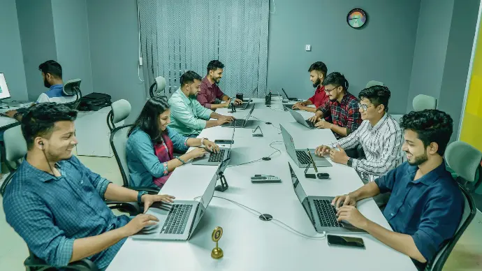 a group of people sitting around a table with laptops